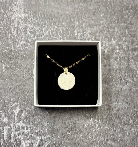 Confezione originale Myra Lab aperta, contenente la collana con pendente tondo bianco con pallini dorati, in porcellana fredda. Gioiello artigianale realizzato da persone cieche e ipovedenti.