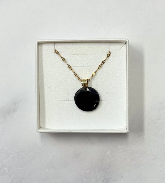 Confezione originale Myra Lab aperta, contenente la collana con pendente tondo nero intenso con glitter, in porcellana fredda. Gioiello artigianale realizzato da persone cieche e ipovedenti.