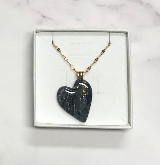 Confezione originale Myra Lab aperta, contenente la collana con ciondolo a forma di cuore, nero con dettagli dorati, in porcellana fredda. Gioiello artigianale realizzato da persone cieche e ipovedenti.