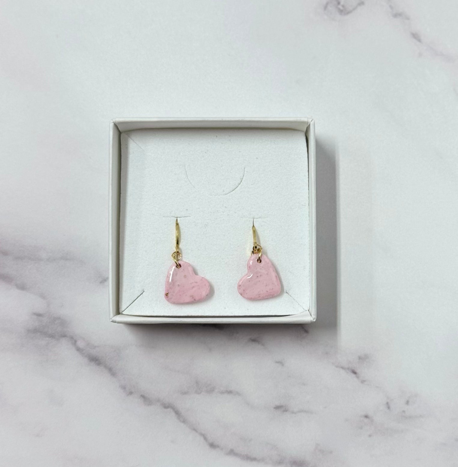 Confezione originale Myra Lab aperta, contenente orecchini con cuore rosa in porcellana fredda. Gioiello artigianale realizzato da persone cieche e ipovedenti.